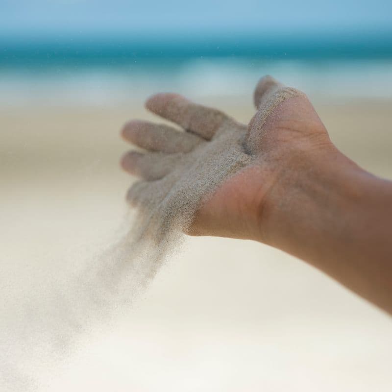 Sand, der løber gennem en åben hånd ved stranden